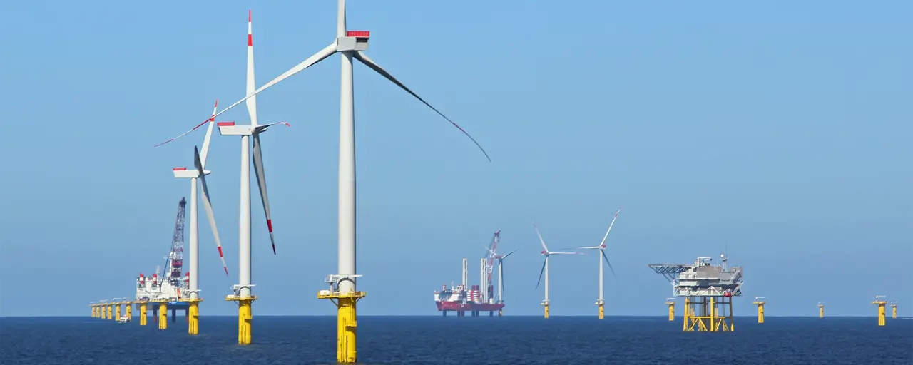 Big white wind turbines in sea water against blue sky.