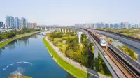 Picture of train going over water stream and fields with city in the background.