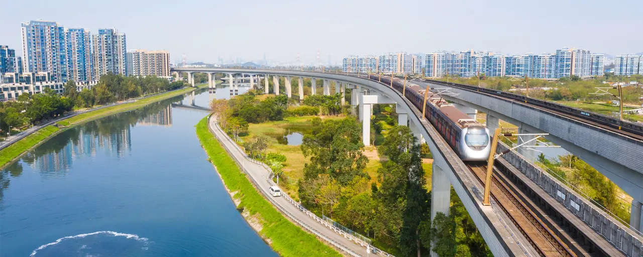 Picture of train going over water stream and fields with city in the background.