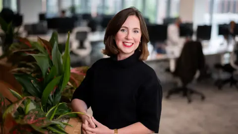 Portrait of Lydia Parnell, Director, Global Corporate Responsibility, standing in office space against plant.