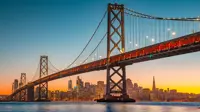 Panoramic view of San Francisco skyline with famous Oakland Bay Bridge illuminated in beautiful golden evening light at sunset in summer