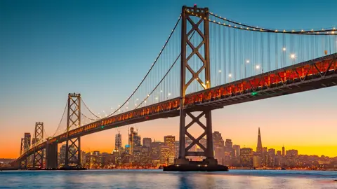 Panoramic view of San Francisco skyline with famous Oakland Bay Bridge illuminated in beautiful golden evening light at sunset in summer