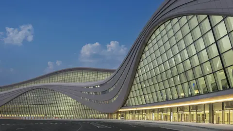 The exterior of Zayed International Airport, a glass front airport terminal against a blue evening sky 